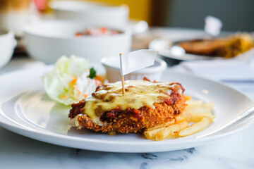A serving of crispy chicken parmigiana or schnitzel topped with melted cheese, served with french fries and a salad on a white plate