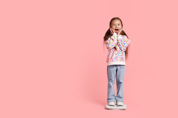 Naklejka premium Little girl standing on scales against pink background, space for text