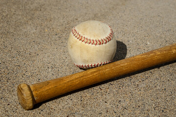 closeup of a wooden baseball bat and a white baseball with red stitching isolated on a textured concrete surface with copy space. sports and nostalgia background or design element banner.