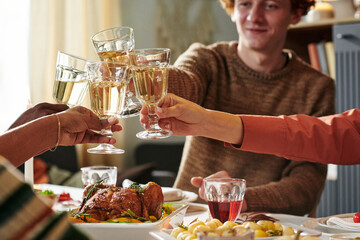 Diverse group of young adults raising wine glasses in toast around Thanksgiving dining table, celebrating together with roasted chicken and assorted dishes visible