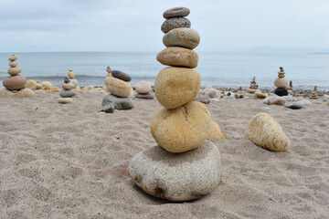 Artistic stone stacks of various sizes arranged on the sandy beach with the ocean in the background in Puerto Vallarta, Jalisco