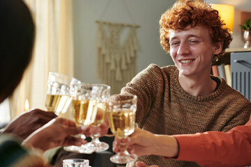 Caucasian young adult man smiling while clinking glasses with diverse group of people during social gathering, holding glass of wine, celebrating together at indoor event