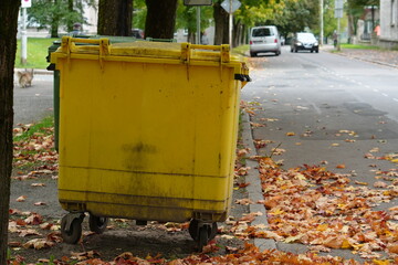Large Yellow Waste Bin on Urban Street Curb with Autumn Leaves