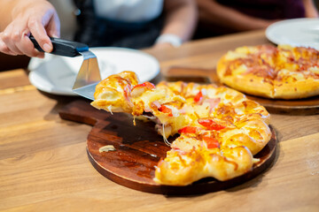 Close up of a person serving hot cheese pizza with a spatula in a restaurant. Freshly baked pizza topped with melted cheese and toppings, ideal for food, dining, and Italian cuisine concepts.