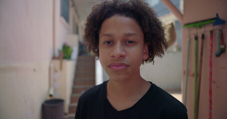 Hispanic teenage Latin boy of African descent standing casually in suburban alleyway, showing calm...
