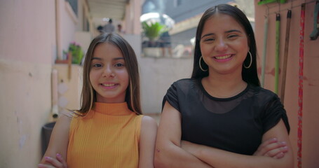 Two young Hispanic Latin girls smiling together in suburban alleyway, cheerful and friendly,...