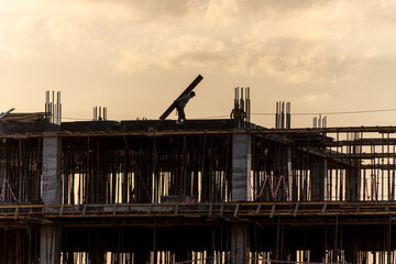 A silhouette of a construction worker carrying a wooden beam on a building site against a cloudy, golden sky at sunset. The image captures the hard work and progress of the construction industry.
