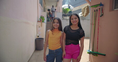 Two young Hispanic Latin girls smiling together in suburban alleyway, cheerful and friendly,...