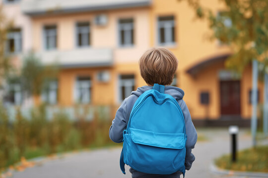 Little boy with blue backpack walking to school building on a sunny autumn day - Powered by Adobe