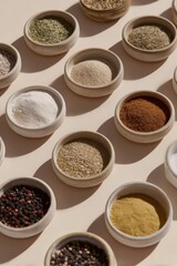 Multiple small ceramic bowls containing a variety of ground and whole spices are arranged in diagonal rows casting soft shadows on a beige background