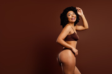 Fototapeta premium Beautiful young woman in elegant brown lingerie posing gracefully against a warm monochromatic background