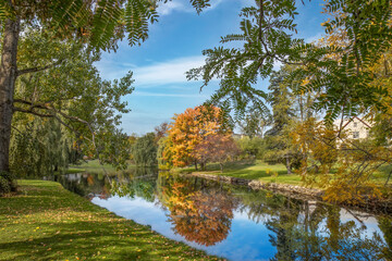 Small calm lake in an urban park during autumn showing trees with fall foliage, reflections, daytime, sunny, nobody