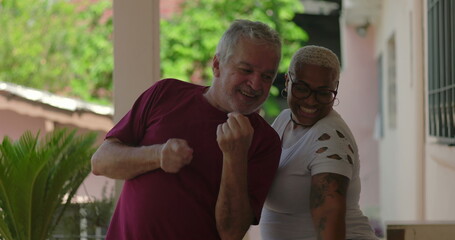 Elderly man and a cheerful Black woman dancing joyfully in a vibrant outdoor gathering,...