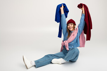 Joyful young woman showcases colorful warm clothes with playful energy in a bright setting