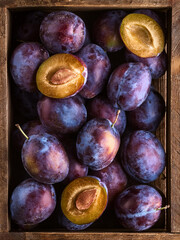 Fototapeta premium A wooden crate filled with ripe, purple plums. The plums are arranged inside the crate on a wooden surface.