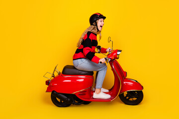 Cheerful young woman riding a red scooter against a yellow background exudes a carefree and stylish...