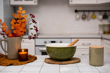 In a warm kitchen, a green bowl is surrounded by autumn leaves and soft lighting, creating a cozy...