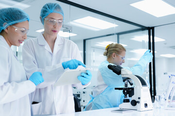 A senior scientist mentors a junior colleague in a modern lab, using a tablet to guide her through a precise pipetting technique, fostering hands-on learning and skill development.