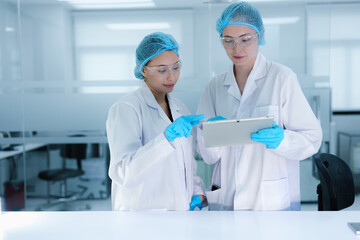 A senior scientist mentors a junior colleague in a modern lab, using a tablet to guide her through...