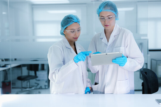 A senior scientist mentors a junior colleague in a modern lab, using a tablet to guide her through a precise pipetting technique, fostering hands-on learning and skill development.