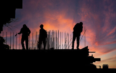 Workers construct a building on a construction site against a vibrant sunset sky
