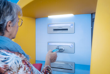 Senior woman using an automated ticket machine inserting a bank card for payment. Concept of modern technology, digital transaction, independence, elderly person managing financial tasks independently