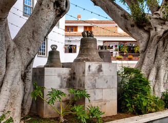 Old bells beside the church Nuestra Senora de Fatima in Santa Brigida, Gran Canaria between trees and traditional buildings.