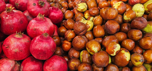 Ripe pomegranates and jujube fruits are piled side by side at a Spanish market stall, creating a colorful and fresh contrast. seasonal produce