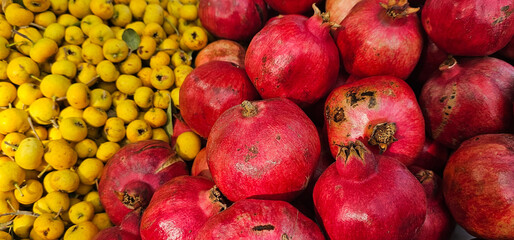 Bright red pomegranates and small yellow loquats are displayed side by side at a Spanish market,...