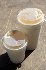  There is a paper cup with coffee and tea on the wooden table.