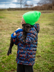 Joyful boy holding black baby goat on farm. Rural lifestyle, childhood, and animal care in countryside setting. Happy childhood