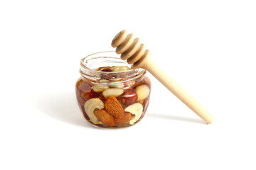 On a white background there is a glass jar filled with honey and nuts.	