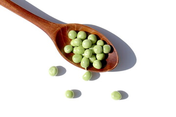 On a white background lies a wooden spoon with fresh green peas.	