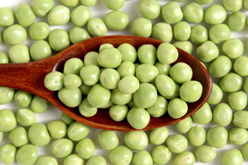 On a white background lies a wooden spoon with fresh green peas.	