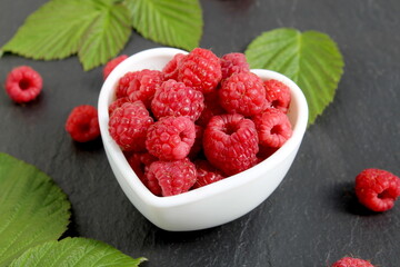 Red ripe raspberries lie in a bowl on a black background.	