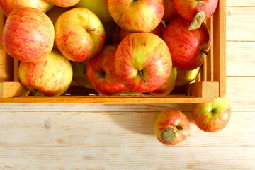 There is a box of fresh red apples on a wooden background.