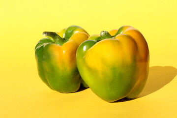 On a yellow background there are two yellowing sweet peppers.