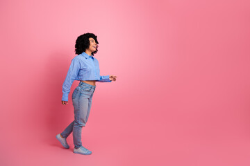 Smiling young woman with curly hair walking confidently in casual attire against vibrant pink...