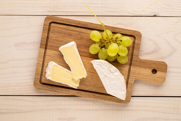 Fragrant camembert cheese with grapes on a wooden table, top view.