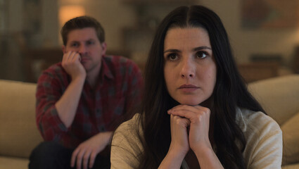 Fototapeta premium Upset woman sitting on a couch with her partner in the background during a difficult conversation at home. 