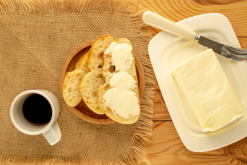 Butter in a white ceramic butter dish with slices of bread on a wooden table, top view.