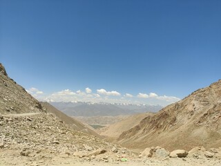 A breathtaking view of rocky Himalayan mountains under a clear blue sky with scattered clouds, showcasing natural beauty and serene high-altitude landscape.
