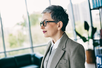 Confident mature businesswoman smiling indoors in a modern office space with stylish formalwear and natural lighting