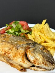 A close-up shot of fried potatoes, fried fish, and a salad with fresh vegetables and herbs. Cooking delicious food at home.