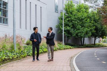 Two young professional men walking and conversing outdoors on a college campus