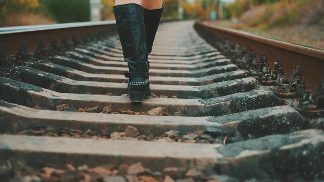 Close-up shot legs walking along railroad track, feet stepping on sleepers, unrecognizable silhouette person in grunge black boots, rocker style with chains, back rear view woman goes on adventure 4k