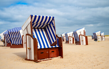 Typical beach chairs with blue and white striped cushions on the sandy beach of Norderney invite you to relax and sunbathe. A vacation idyll on the North Sea (Germany)