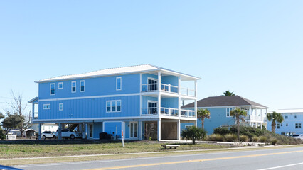 Fototapeta premium Blue beach house with balconies and palm trees near road in sunny coastal environment