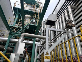Close-up view of industrial steel pipelines, valves, and structural support in a modern chemical or petroleum refinery plant. Detailed view of industrial equipment and machinery with a warning sign 