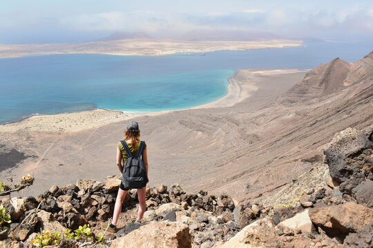Woman hiker exploring dramatic volcanic Lanzerote coastline and turquoise ocean views on La Graciosa island during sunny adventure travel in the Canary Islands